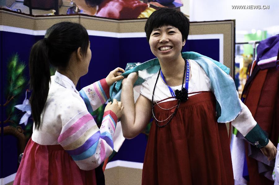 A visitor tries on traditional Korean costume at the Beijing International Tourism Expo (BITE) 2013 in Beijing, capital of China, June 21, 2013. The BITE 2013 kicked off on Friday, attracting 887 exhibitors from 81 countries and regions. [Photo: Xinhua/Liu Jinhai] 