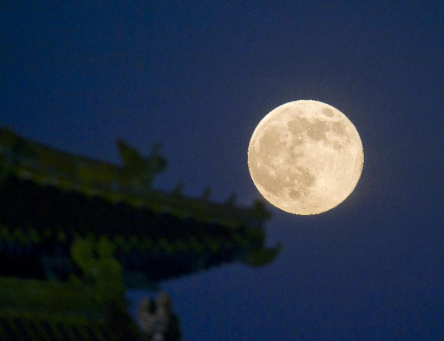 A full moon sets behind a building of the Forbidden City in Beijing, capital of China, June 23, 2013. The moon looks 14 percent larger and 30 percent brighter than usual on Sunday. The scientific term for the phenomenon is "perigee moon", but it is also known as a "super moon". (Xinhua/Chen Duo) 