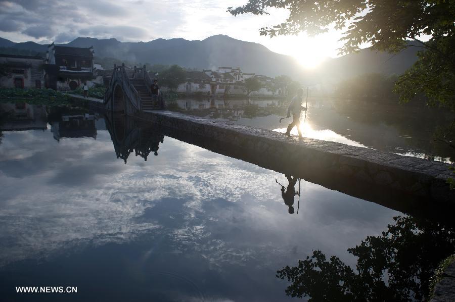 A local resident leaves Hongcun, an ancient village founded in 1131, for farm work, in Huangshan City, east China's Anhui Province, early July 3, 2013. Listed as a world cultural heritage site, the village preserved to a remarkable extent the surviving examples of Anhui-style architecture and traditional lifestyle. (Xinhua/Guo Chen) 