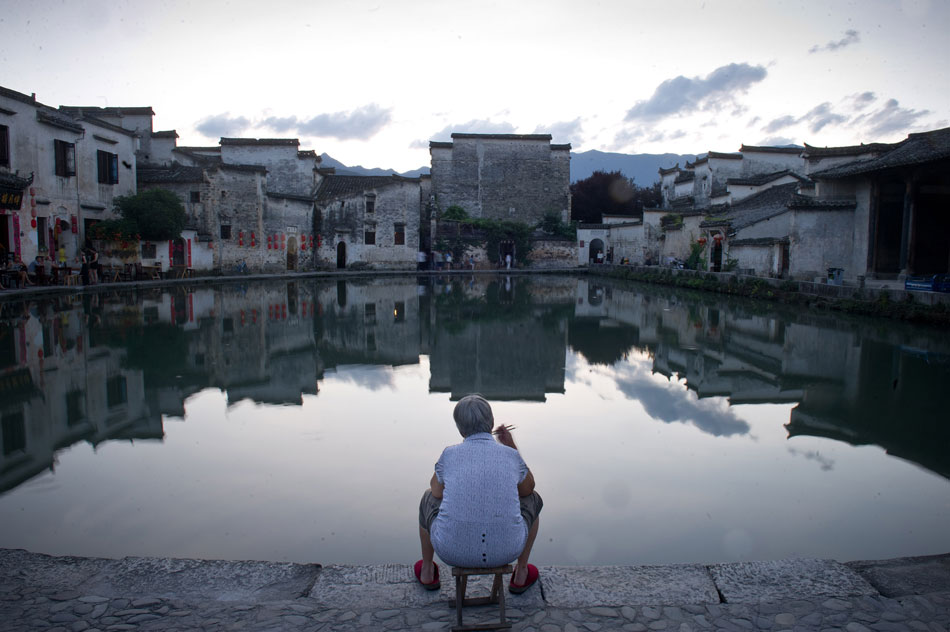 The photo taken on July 2 shows a local resident who has her supper besides a pond in 900-year-old Hongcun old town, in east China's Anhui province. (Xinhua/Guo Chen)