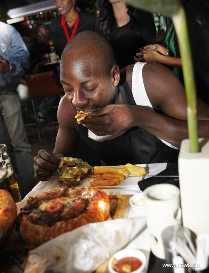 A contestant takes part in a burger challenge at Brew Bistro in Nairobi, capital of Kenya, July 9, 2013. Four contestants had one hour to finish a 5kg burger with beef, two huge burger buns and 40 toppings. Sauti Sol team won the burger challenge. (Xinhua/Li Jing)