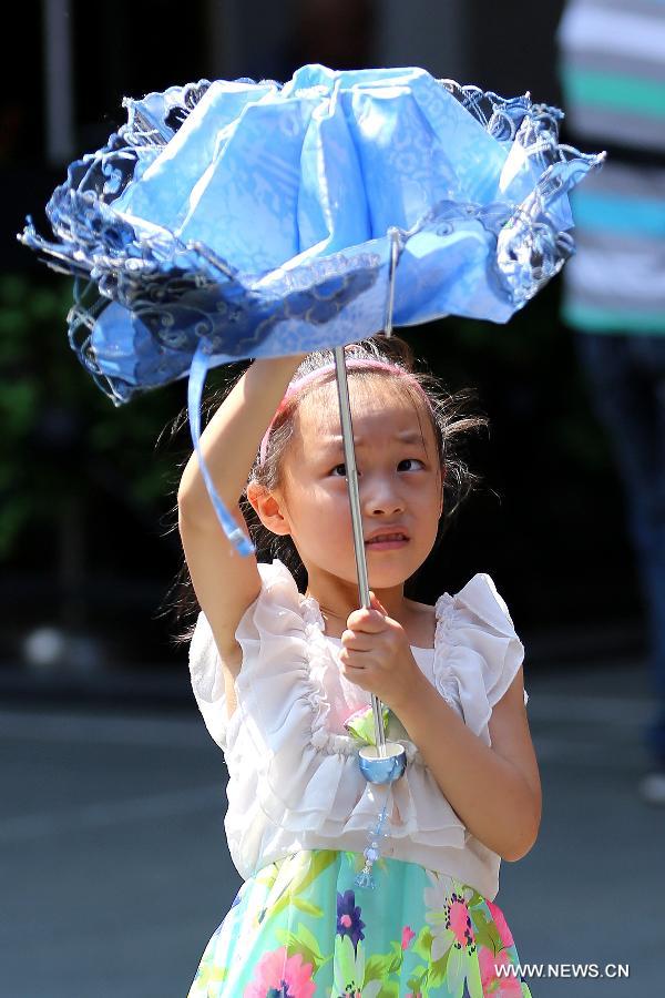 A child prepares to open an umbrella to shade herself from the sun in Shanghai, east China's municipality, July 15, 2013. Local meteorological observatory issued an yellow-coded alert of heat at noon on July 15, 2013.(Xinhua/Yang Shichao) 