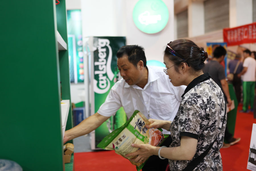 Hu Zhengming (left), marketing manager of a green food company selling lotus roots products in east China's Jiangsu province, introduces their products to visitors at the 2013 China International Consumer Products Exhibition. [Photo: CRIENGLISH.com/Wang Wei] 