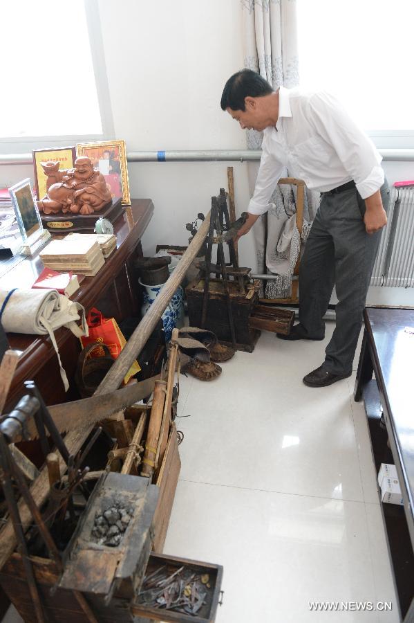 A man points to tools the village museum collected in Yanzhangzi Village of the Man Autonomous County of Kuancheng, north China's Hebei Province, July 16, 2013. A museum collecting old stuff was set up in the village to remind the local residents of hard time in the old days. (Xinhua/Wang Min)