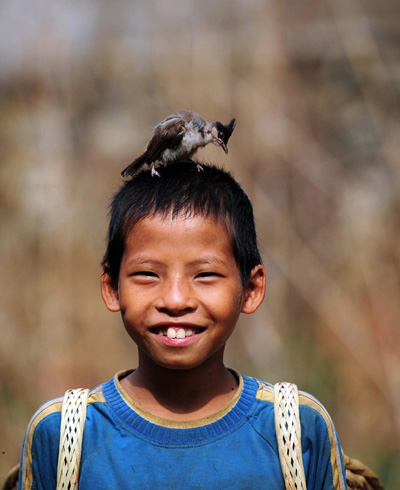 A boy plays with a bird while carrying corn in the Dahua Yao ethnic county of Guangxi Zhuang autonomous region on July 14, 2013. (Photo/Xinhua)