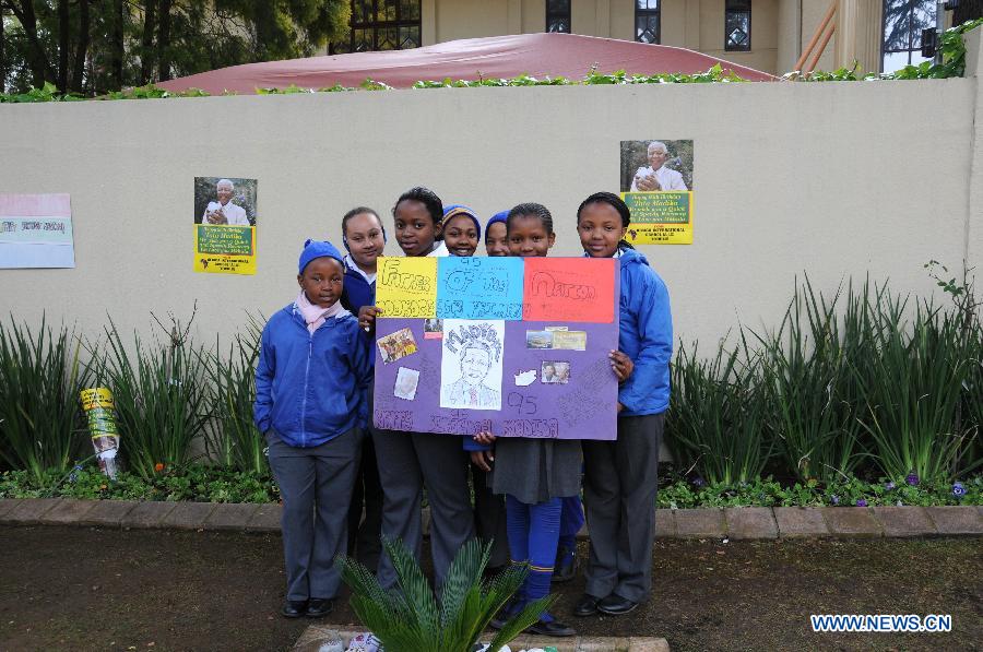 Students show a card with wishes outside Mandela's house in Johannesburg, South Africa, on July 18, 2013. South African former president Mandela is steadily improving, according to the Presidency website update released on Thursday. "Madiba remains in hospital in Pretoria but his doctors have confirmed that his health is steadily improving," said the statement. President Jacob Zuma wished the founding father of the nation a happy 95th birthday. (Xinhua/Guo Xinghua)