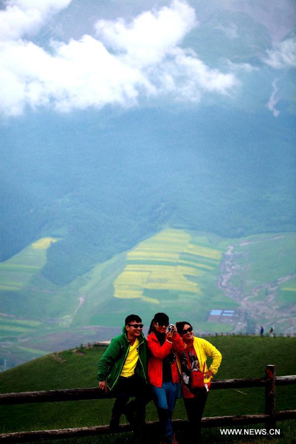 Tourists pose for photos at Zhuo'er Mountain in Qilian County, northwest China's Qinghai Province, July 16, 2013. The tourist attraction witnessed a travel peak in July with its snow mountains and blossoming rape flowers. (Xinhua/Yang Shoude)