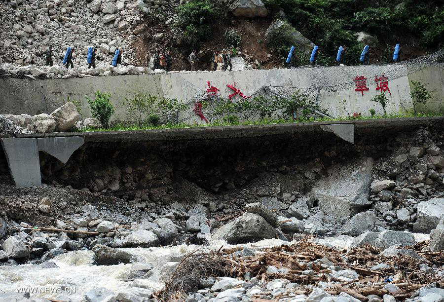 Relief workers carry disaster-relief supplies on the restored road in Caopo Township of Wenchuan County, southwest China's Sichuan Province, July 20, 2013. The road lingking Caopo Township and outside which was badly damaged by previous mud-rock flow has been reopened on Saturday, which will facilitate future rescue work in the town.(Xinhua/He Haiyang)