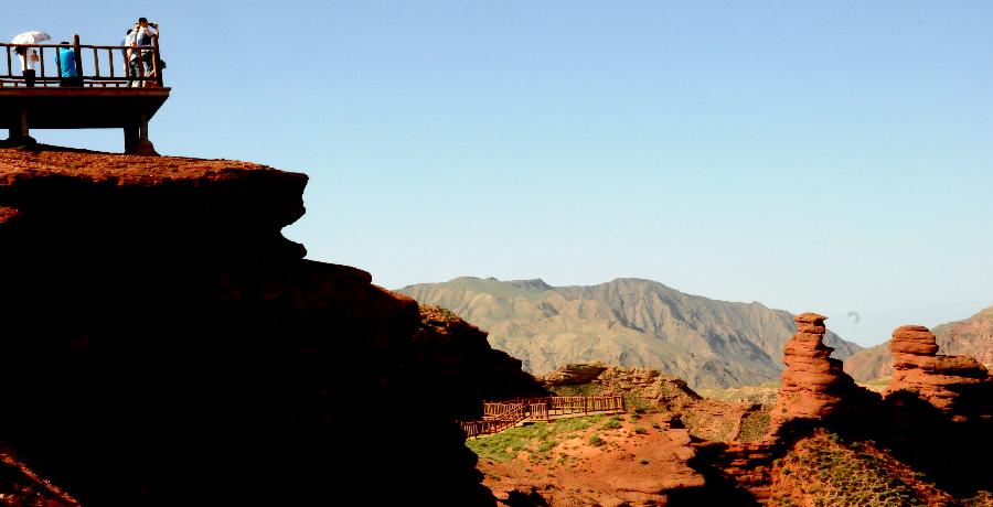 Visitors view the scenery of Danxia landform at Pingshan Lake scenic area in Zhangye City, northwest China's Gansu Province, July 20, 2013. Danxia, which means "rosy cloud", is a special landform formed from reddish sandstone that has been eroded over time into a series of mountains surrounded by curvaceous cliffs and many unusual rock formations. (Xinhua/Wang Jiang)