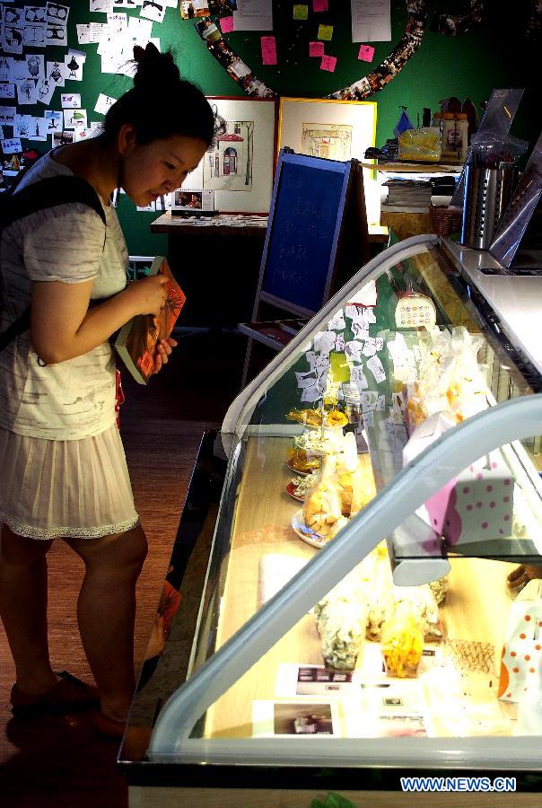 A customer selects bread in an entity bookstore on Changshu Road in east China's Shanghai, July 21, 2013. Some new style entity bookstores in Shanghai are opened with beverage, food supply and stationery selling. These customer-oriented bookstores bring a new idea for selling books and attract many customers to spend time on reading here. (Xinhua/Chen Fei)