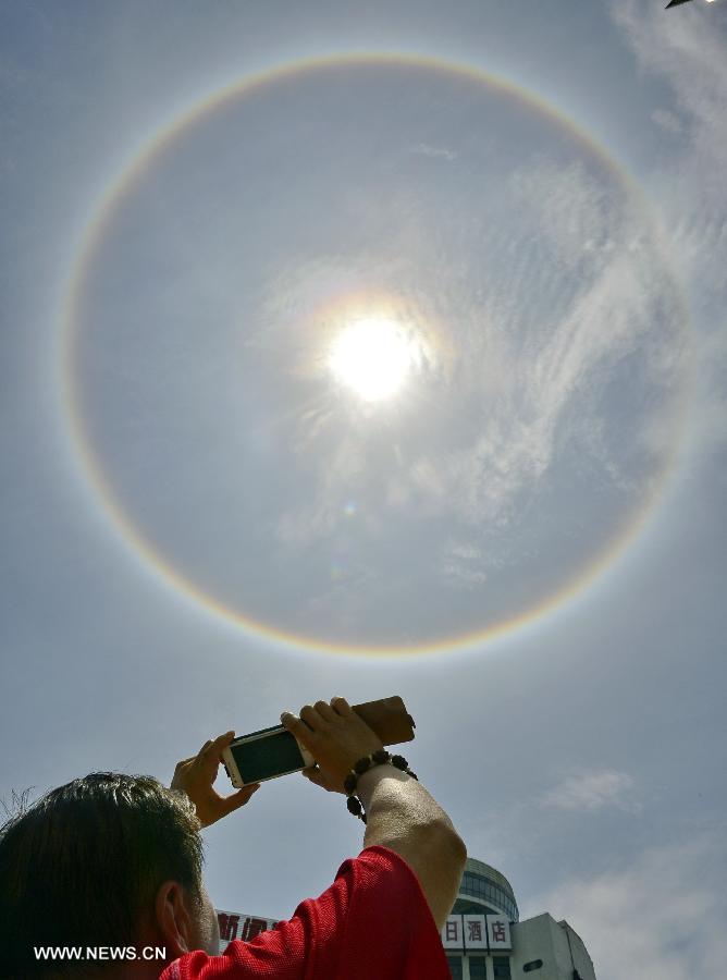A passer-by takes photos of solar halo with mobile phone in Qinhuangdao City, north China's Hebei Province, July 22, 2013. (Xinhua/Liu Xuezhong)