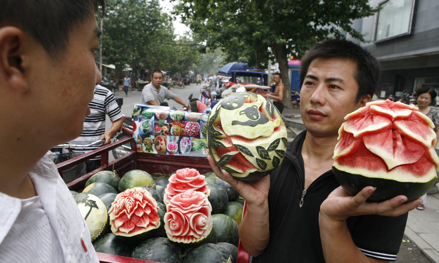 Zhang Yunxiao, a 30-year-old fruit dealer, tries to sell artistic watermelons to a customer in Xiangyang, Hubei province, on Monday, July 23, 2013. Zhang carves vivid flowers like peonies and roses as well as other patterns on the melons. The price for each melon is 20 yuan ($3.26) to 50 yuan. (Photo / China Daily)