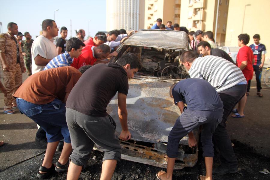 Libyans gather at a burnt vehicle which was destroyed by a rocket fired towards a residential building in Tripoli, July 23, 2013. The rocket was fired at the neighborhood of western embassies housing buildings and companies when it was empty at the moment of explosion. (Xinhua/Hamza Turkia)