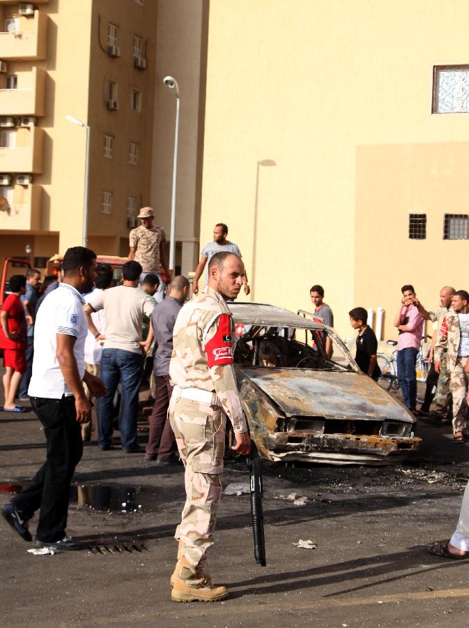 Libyans gather at a burnt vehicle which was destroyed by a rocket fired towards a residential building in Tripoli, July 23, 2013. The rocket was fired at the neighborhood of western embassies housing buildings and companies when it was empty at the moment of explosion. (Xinhua/Hamza Turkia) 