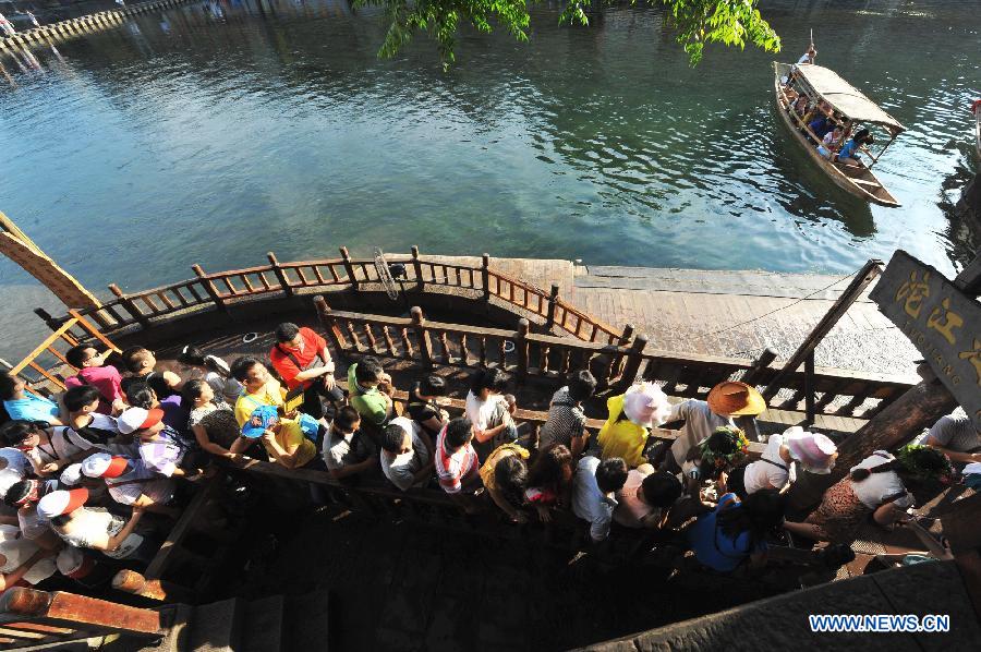 Tourists wait to board boats beside the Tuojiang River in the ancient town of Fenghuang in Fenghuang County of Xiangxi Tu and Miao Autonomous Prefecture, central China's Hunan Province, July 23, 2013. The tourist resort witnessed a travel peak in July, attracting 417,400 visitors till July 22, increasing by 28.79 percent year on year. (Xinhua/Long Hongtao)