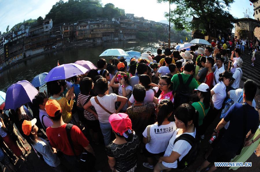 Tourists wait to board boats beside the Tuojiang River in the ancient town of Fenghuang in Fenghuang County of Xiangxi Tu and Miao Autonomous Prefecture, central China's Hunan Province, July 23, 2013. The tourist resort witnessed a travel peak in July, attracting 417,400 visitors till July 22, increasing by 28.79 percent year on year. (Xinhua/Long Hongtao)