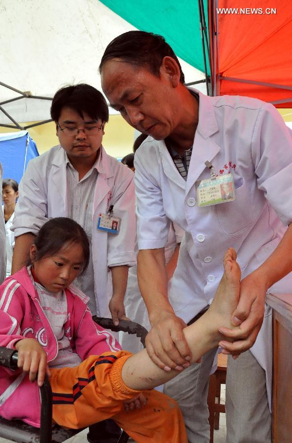 A doctor checks the condition of a child's leg in a makeshift clinic in Meichuan Town of Minxian County, northwest China's Gansu Province, July 24, 2013. By far, makeshift clinics have been set up to offer basic medical treatment in quake-hit towns. And severely injured people have been sent to hospitals for better care in the county seat of Minxian, Dingxi City and Lanzhou City, capital of Gansu. (Xinhua/Guo Gang)  