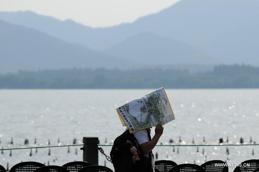 A tourist holds a map for shelter beside the West Lake in Hangzhou, capital of east China's Zhejiang Province, July 25, 2013. The highest temperature in Hangzhou reached 40.3 degrees Celsius on Thursday. (Xinhua/Ju Huanzong)