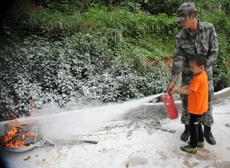 An instructor teaches a little boy to use fire extinguisher at the provincial youth fire control and protection education base in Kunming, capital of southwest China's Yunnan Province, July 30, 2013. More than 80 migrant children in Kunming participated in a summer camp, which lasts from July 29 to Aug. 1, where they can learn knowledge related with transportation safety, fire control and earthquake protection at the base. (Xinhua/Qin Lang) 