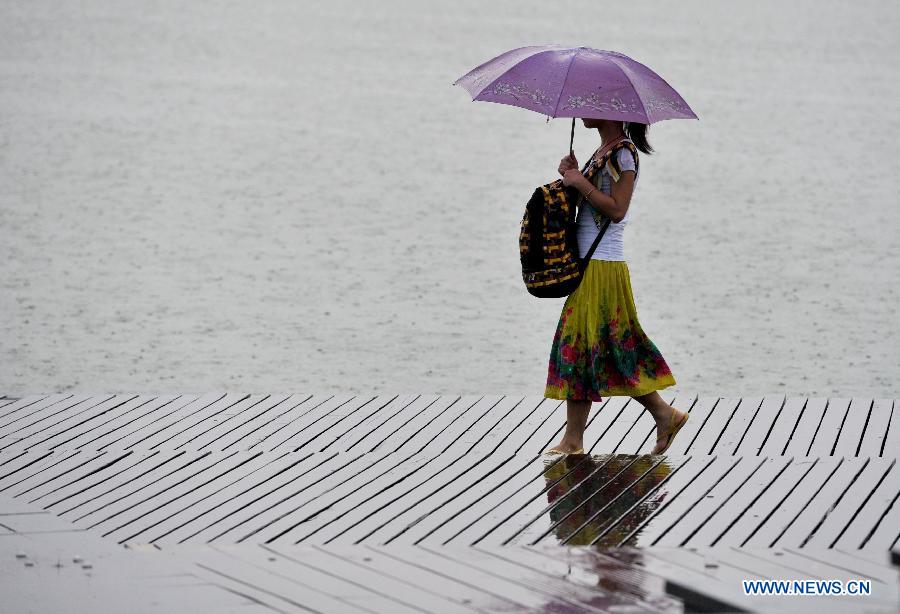 A citizen walks in the rain beside the Xuanwu Lake in Nanjing, capital of east China's Jiangsu Province, July 31, 2013. An artificial precipitation brought coolness to citizens in Nanjing. (Xinhua/Lang Congliu)