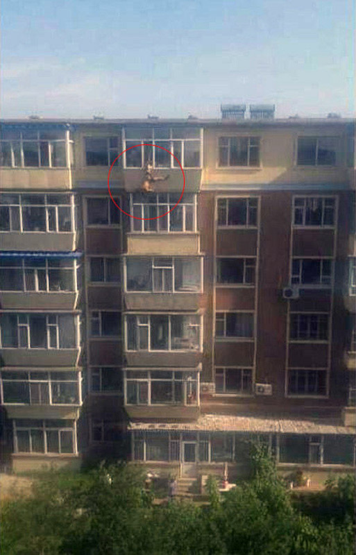 A man tries to jump from the building to commit suicide in a residential area in Changchun, captial of China's Jilin Province, July 31, 2013. While he jumped out of the window, his leg was caught by his wife. Later he was rescued by the neighbors and policemen. (Photo/Xinhua)