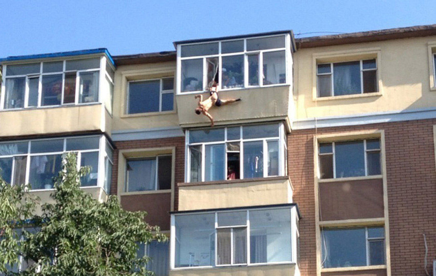 A man tries to jump from the building to commit suicide in a residential area in Changchun, captial of China's Jilin Province, July 31, 2013. While he jumped out of the window, his leg was caught by his wife. Later he was rescued by the neighbors and policemen. (Photo/Xinhua)